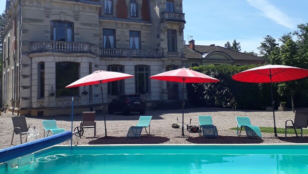 A large building with a swimming pool, red umbrellas, and lounge chairs.
