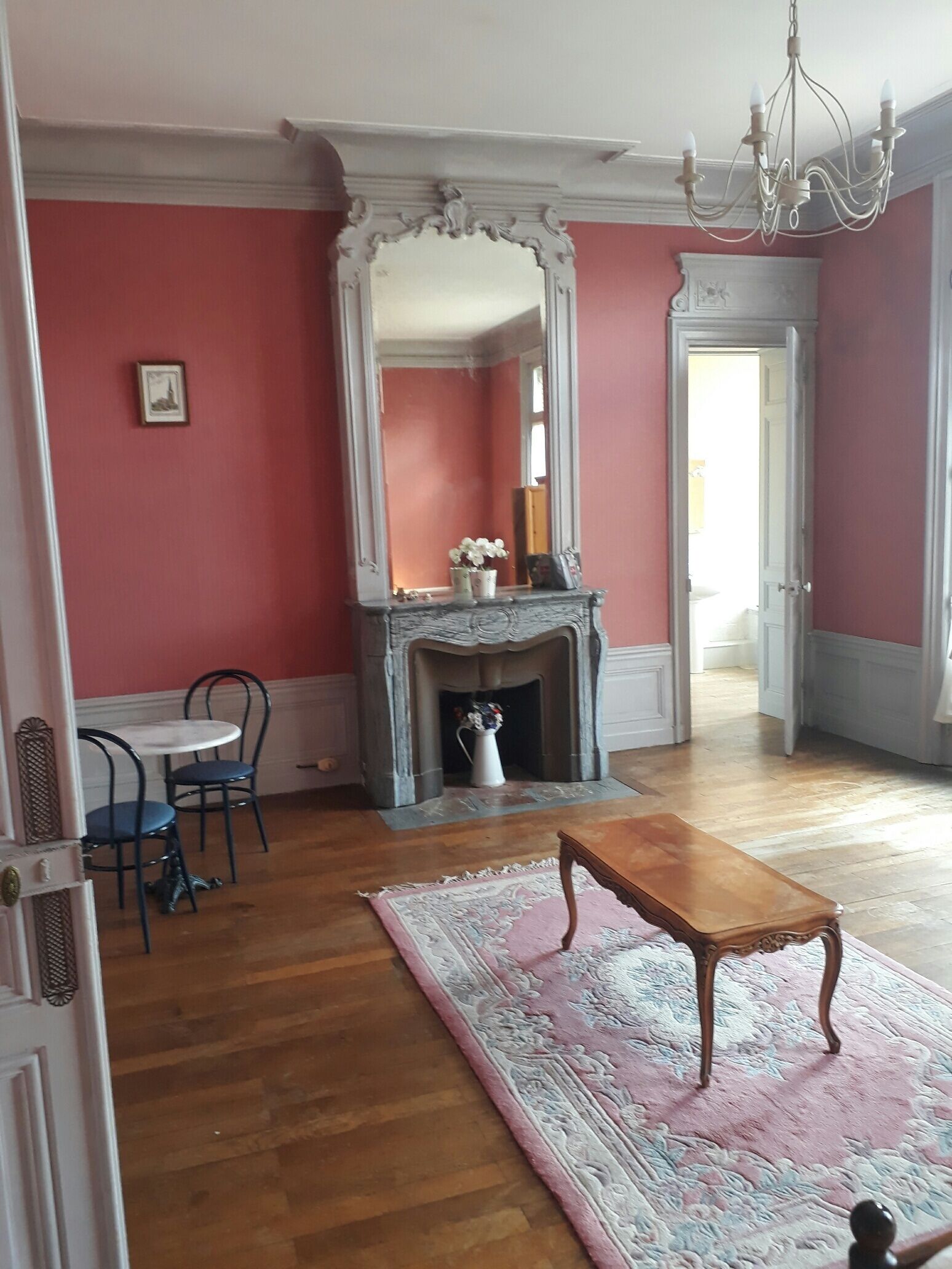 Une pièce avec une cheminée, un miroir, une table et une chaise.