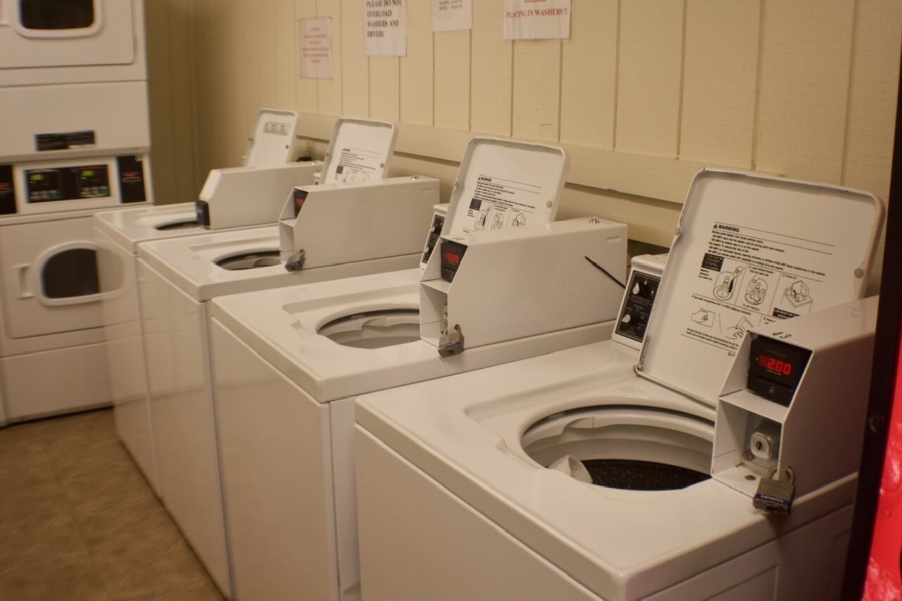 A row of front-loading washing machines in a laundry room with instructional signs on the wall.