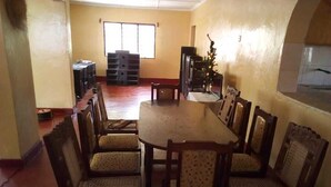 A dining area with a round table and eight chairs, a window with blinds, and a small Christmas tree. - Maui Palm house, Ukunda, 4 bedroom  secure compound, 10 minutes  to the beach. (Ukunda)