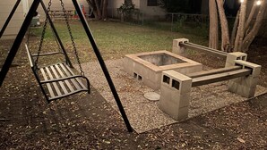 A swing set and a concrete fire pit in a backyard.