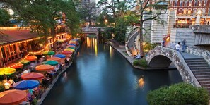 A canal with a stone bridge and a restaurant with colorful umbrellas along the water.