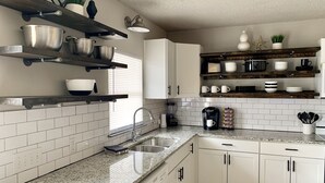 A modern kitchen with white cabinets, granite countertops, and wooden shelves.