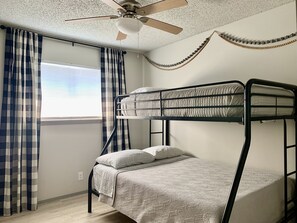 A bunk bed room with a ceiling fan, checkered curtains, and a window with blinds.