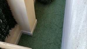 Una esquina de una habitación con césped artificial verde, paredes color beige y un pequeño arbusto redondo.