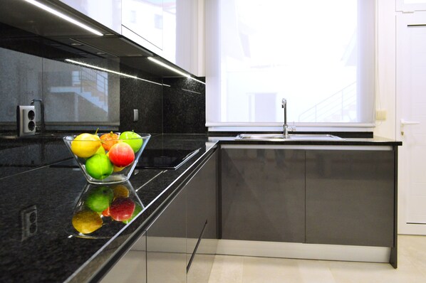 A modern kitchen with a black countertop, a fruit bowl, and a window with a view of buildings. - Casa São Pedro - Caminha (Caminha)