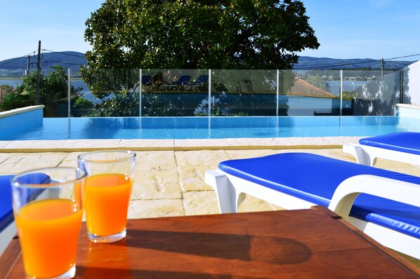 Une vue sur la piscine depuis le bord, avec une vue dégagée sur le bassin, les chaises longues et une table avec des verres de jus d’orange.