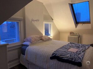 Cozy attic bedroom with a single bed, featuring a white and patterned duvet, and a small window with blinds.