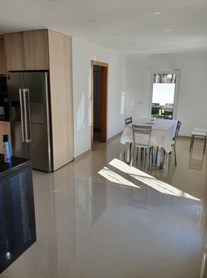 Una cocina moderna con un refrigerador de acero inoxidable, un comedor con mesa y sillas, y vistas al exterior a través de una ventana.