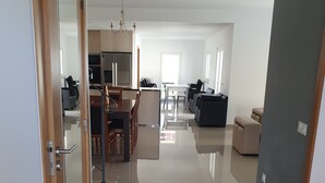A modern living room with a dining area, a kitchen, and a hallway leading to a door. - New house 100 metres from the beach in LAGOA DE ALBUFEIRA (LAGOA DE ALBUFEIRA)