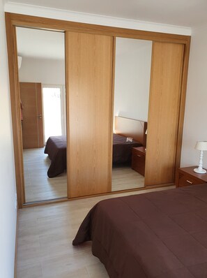 Un dormitorio con un espejo grande, armario de madera y una cama con colcha marrón.
