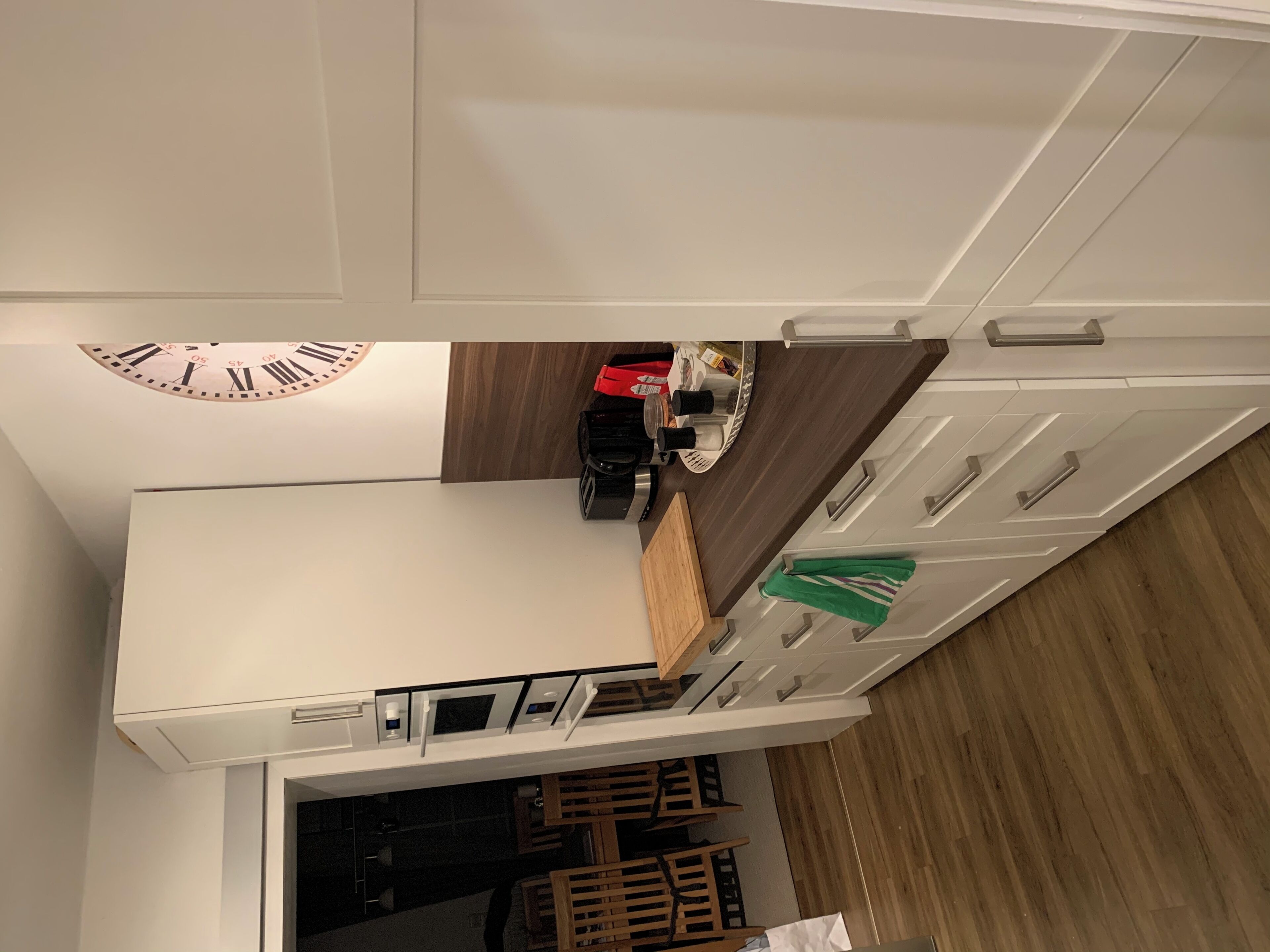 Eine moderne Küche mit weißen Schränken, einer Holz Arbeitsplatte und einer eingebauten Uhr.