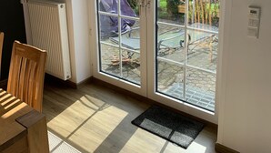 A room with a wooden dining table, a radiator, and a large sliding glass door leading to an outdoor patio with a table and chairs. - Apartment in a beautiful quiet location (Hann. Münden)