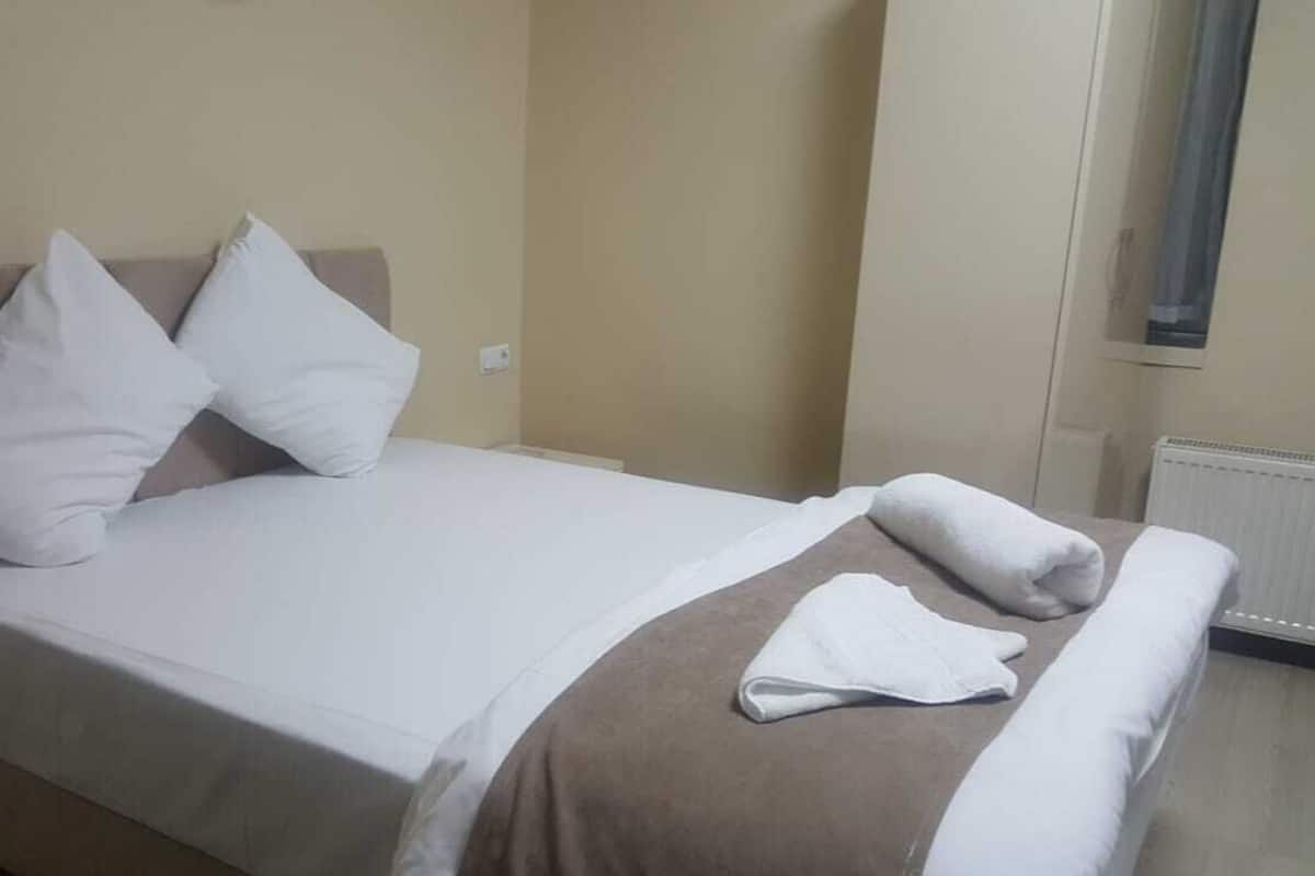 A hotel room with a bed, pillows, a blanket, and a chair.