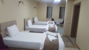 Una habitación de hotel con tres camas individuales, una zona de estar con una silla y un escritorio pequeño.