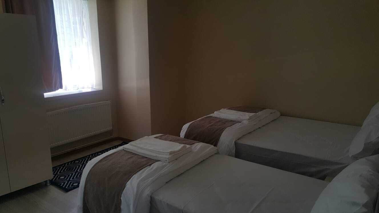 Una habitación con dos camas, un radiador, una ventana con cortinas y una alfombra estampada.