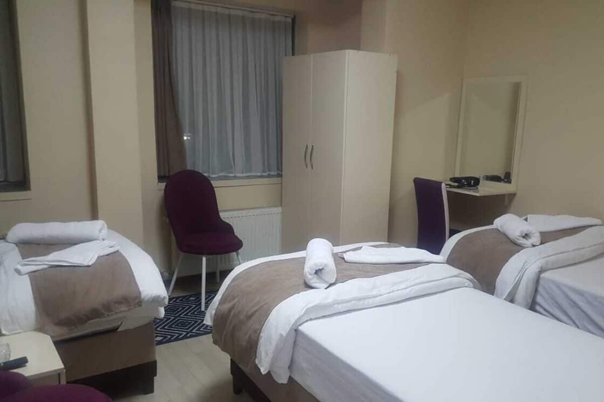 A hotel room with two beds, a desk, a chair, a wardrobe, and a window with curtains.