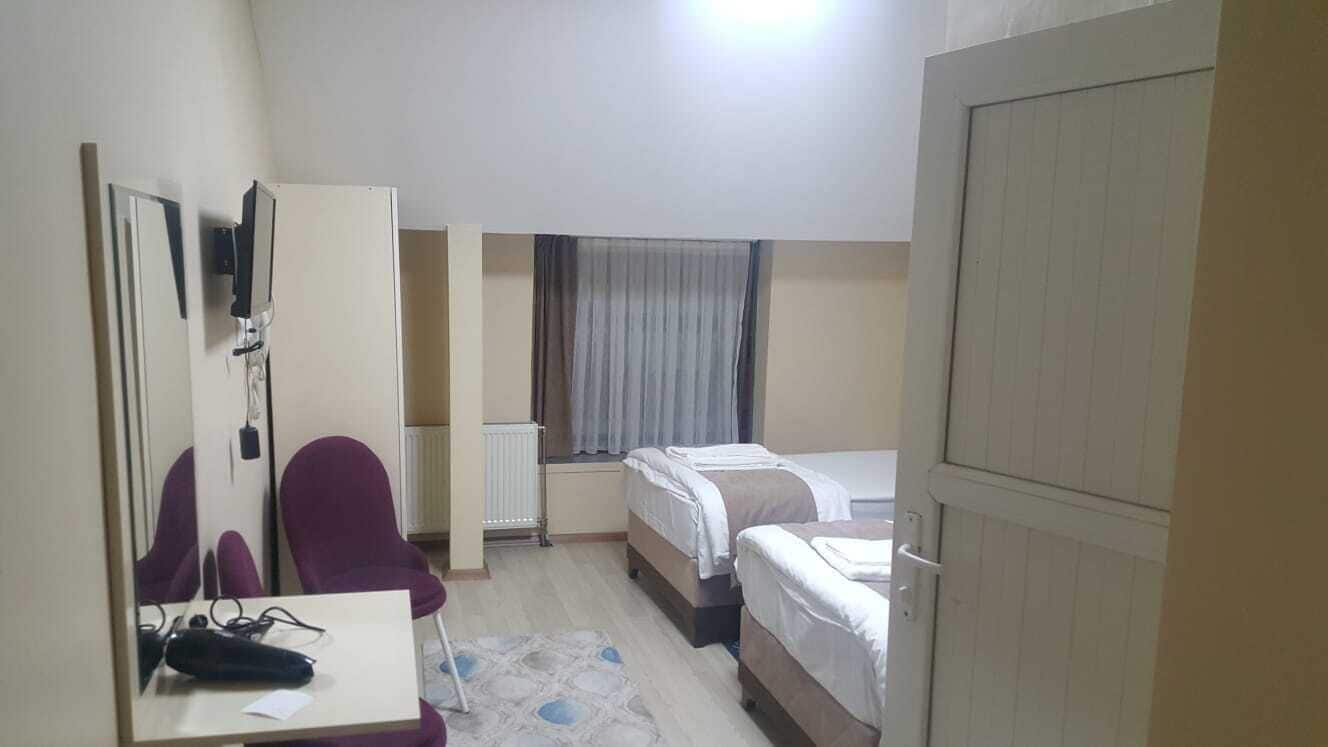 Quarto de hotel com cama, escrivaninha com cadeira, espelho e janela com cortinas.