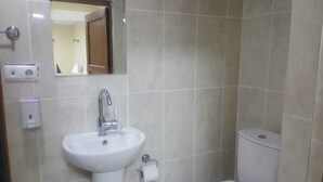 Un baño con lavamanos blanco, espejo, inodoro y enchufe en la pared.