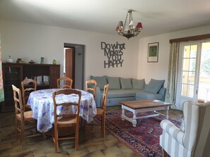 Un salon chaleureux avec une table à manger, des chaises, un canapé et une table basse. On y trouve également une bibliothèque, un lustre et une œuvre d’art murale inspirante.