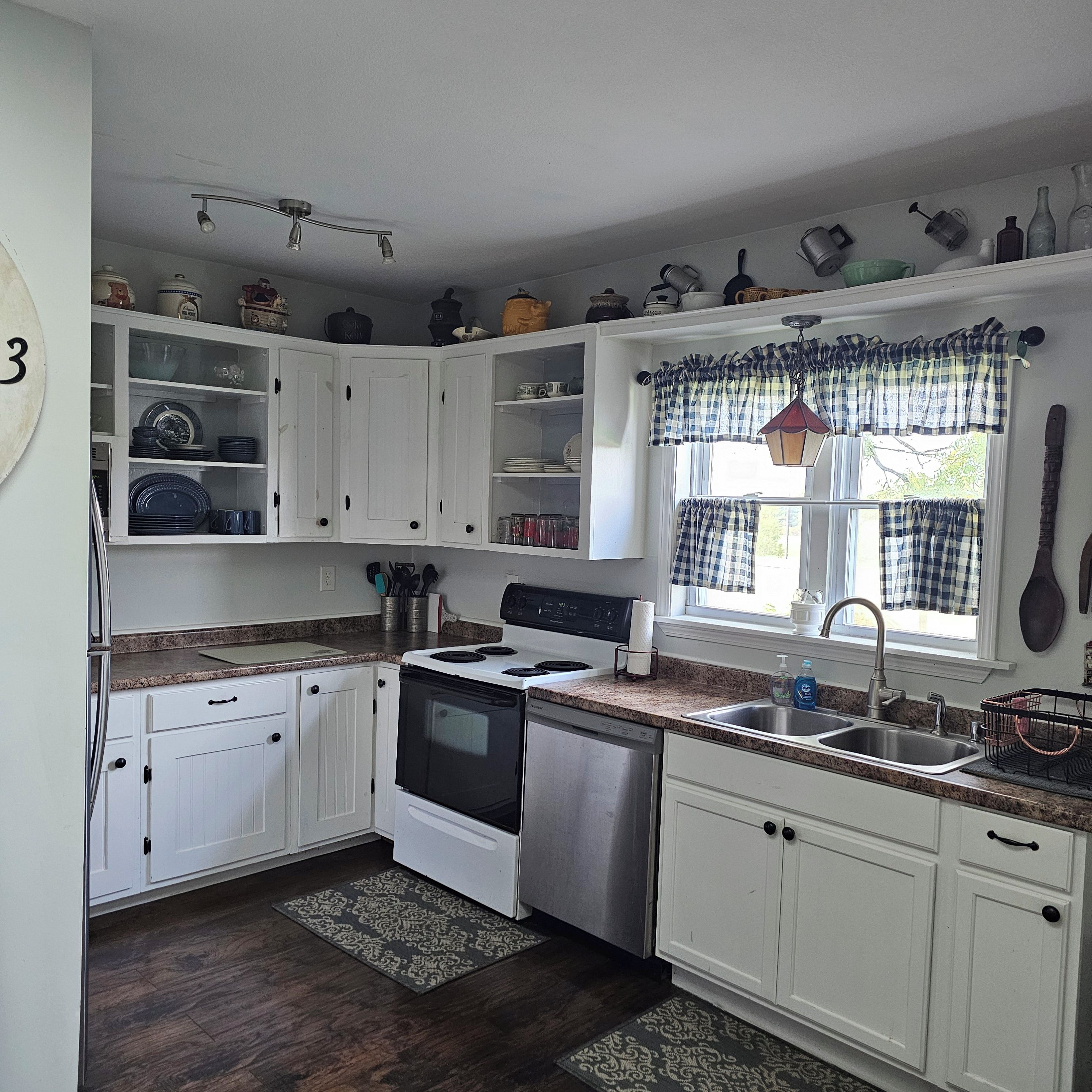 A kitchen with white cabinets, a stove, a dishwasher, and a window with a checkered valance.