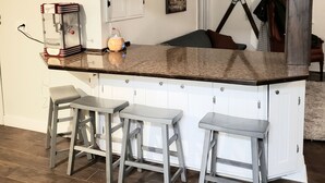 A kitchen with a central island, bar stools, a hanging light fixture, and a painting on the wall.