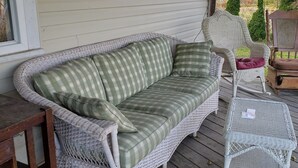 A wicker sofa with a checkered cushion, a matching armchair, and a small table on a wooden deck.