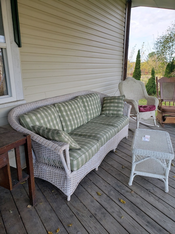 Un canapé en osier avec un coussin à carreaux, un fauteuil assorti et une petite table sur une terrasse en bois.
