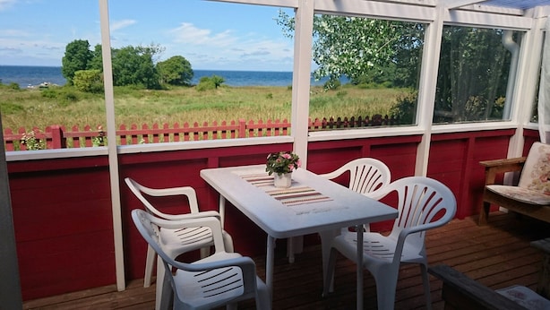 Un patio cubierto con una mesa y sillas, vista al mar y una cerca roja.