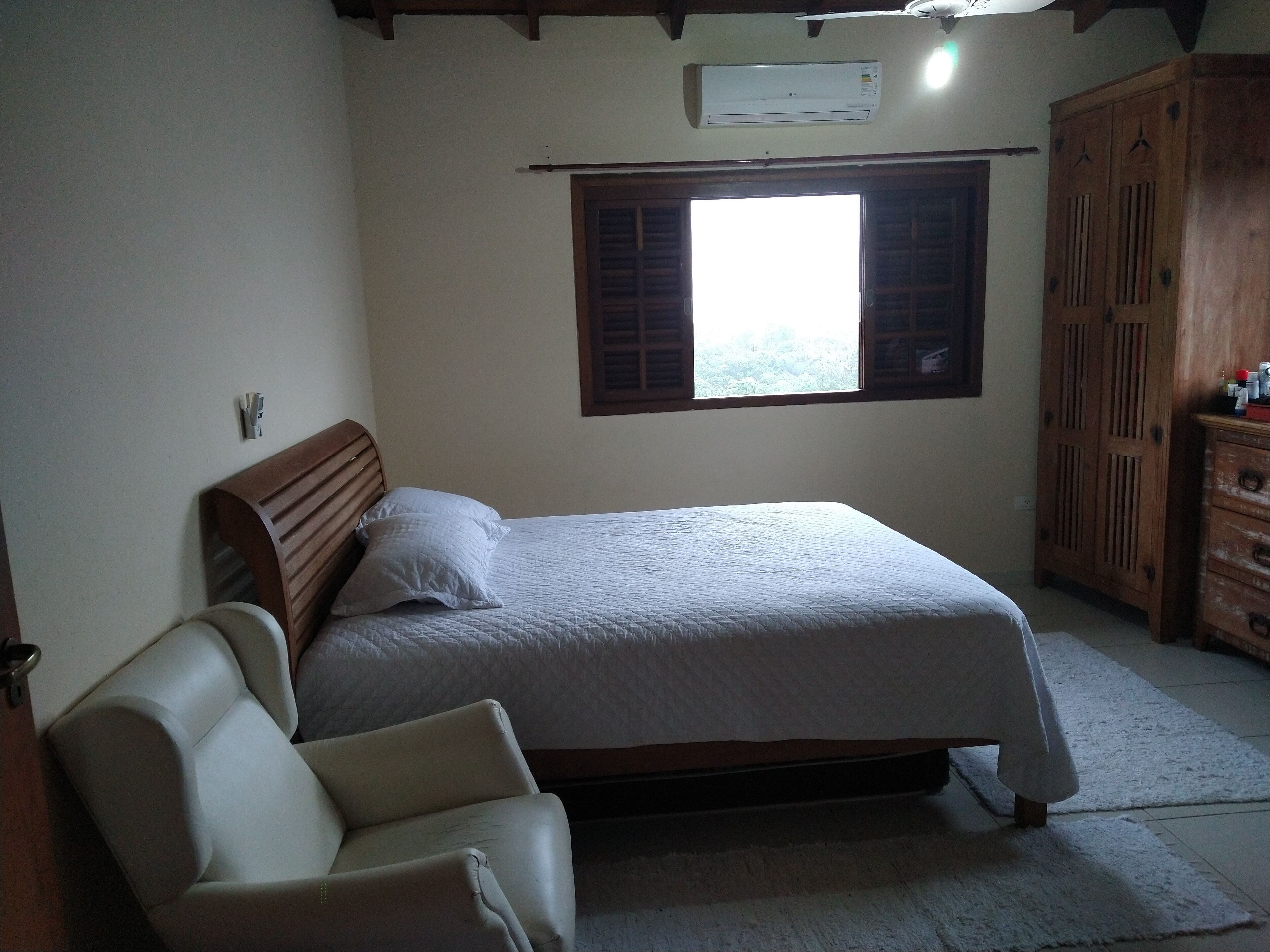 A bedroom with a bed, a wooden wardrobe, a chair, and a window with shutters.