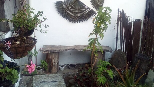 A small garden area with a stone bench, potted plants, and decorative wall art. - Hostal Familiar Jerico (Salento)