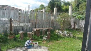 A child playing with a pot in a garden with a wooden fence, trees, and a concrete path. - Hostal Familiar Jerico (Salento)