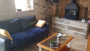 Una sala de estar acogedora con pared de piedra, un sofá azul, una mesa de centro de madera y una estufa de leña.