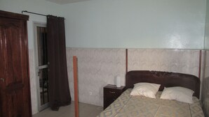 Un dormitorio con cama, mesita de noche, armario de madera y una puerta con cortina.