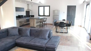 A modern living room with a grey sectional sofa, a wooden coffee table, and a dining area with a table and chairs. - Villa located in the heart of Provence with private pool on 3 hectares. (Roquevaire)