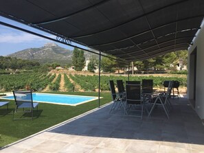 A covered outdoor area with a pool, chairs, and a view of vineyards and mountains.
