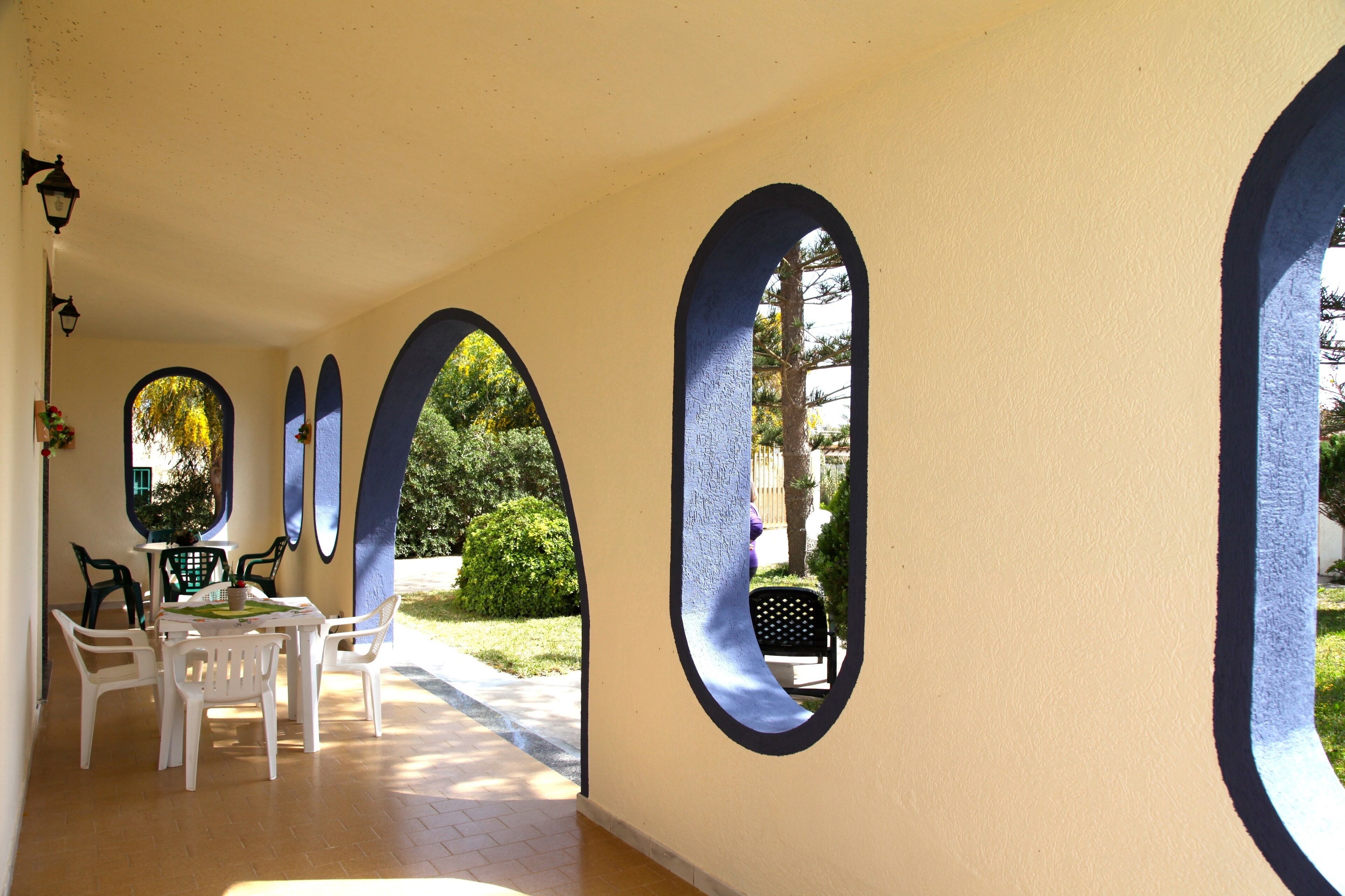 A covered outdoor area with a table and chairs, surrounded by arches with windows.