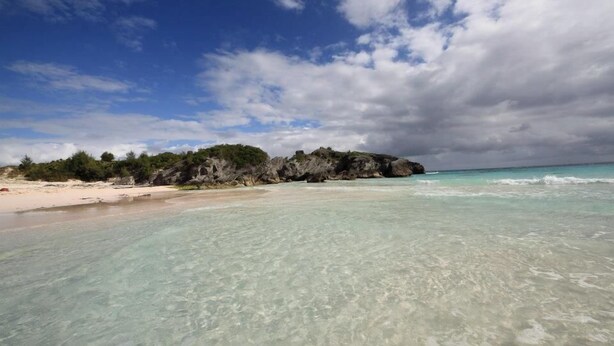 A beach with clear turquoise water, a sandy shore, and a rocky outcrop with greenery. - Your very own private space in Bermuda with Twizy charger (Warwick Parish)