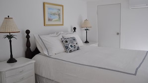 A neatly arranged bedroom with a bed, two bedside lamps, a nightstand, a drawer, and a framed picture on the wall. - Your very own private space in Bermuda with Twizy charger (Warwick Parish)