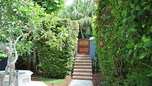 A pathway leading to a wooden door, surrounded by lush greenery and a small garden area. - Your very own private space in Bermuda with Twizy charger (Warwick Parish)