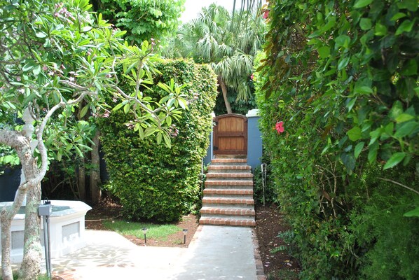 A pathway leading to a wooden door, surrounded by lush greenery and a small garden area.