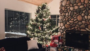 A cozy living room with a wooden ceiling, a stone fireplace, a Christmas tree, and a black sofa with cushions. - Beautiful OHV Friendly Lodge, Sun Room, Close Walk to River, Deck, Fire Pit (South Fork)