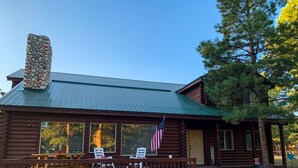 A log cabin with a stone chimney, a porch with chairs, and an American flag. - Beautiful OHV Friendly Lodge, Sun Room, Close Walk to River, Deck, Fire Pit (South Fork)
