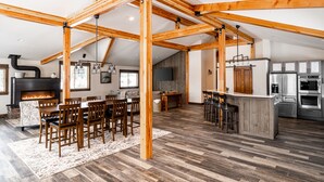 Ein großzügiger Loft-Wohnbereich mit freiliegenden Holzbalken, einem Kamin, einem Esstisch und einer Küche mit modernen Geräten.