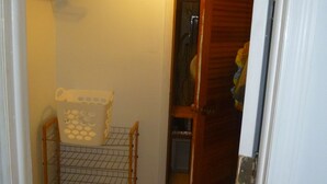 Ein schmaler Flur mit Leopardenmuster-Teppich, einem Drahtregal mit Kartons und einer Holztür zu einem Abstellraum.