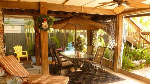 Eine mehrstöckige Holzkonstruktion mit Balkon, einer Hängematte und einem kleinen Gartenbereich mit Pflanzen.