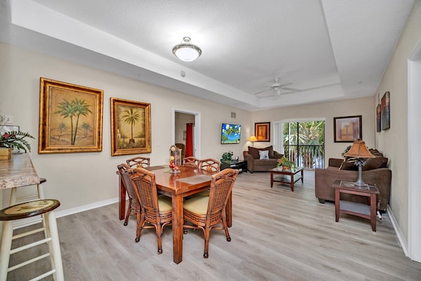 A spacious living area with a dining table, wicker chairs, a sofa, and a TV.