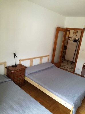 Un dormitorio con dos camas individuales, una mesita de noche de madera con una lámpara y un espejo en la pared.
