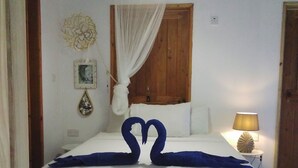 Un dormitorio con una cama, cabecera de madera, lámpara de noche, un cuadro en la pared y una ventana con cortinas.