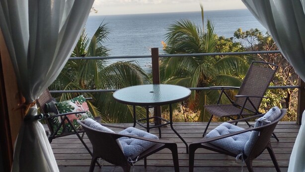Un balcón con mesa y dos sillas, con vista a un cuerpo de agua y palmeras.